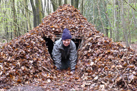 Frontier Bushcraft course student coming out of a natural leaf shelter