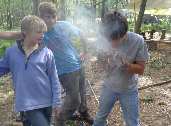 Student blowing a bundle of bracken into flame