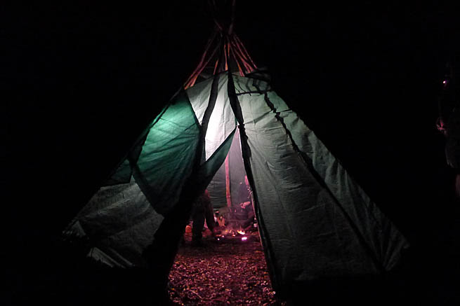 Looking into a warm and cosy tarp tipi shelter from the cold dark outside