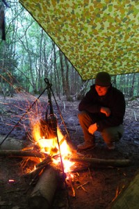 Campfire under a tarp with man crouching next to it