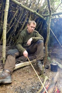 Bushcraft course student inside shelter with only cooking pot, knife and hand-drill