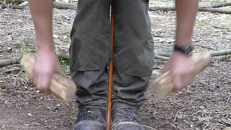Man holding bow saw between feet and knees while running wood against it