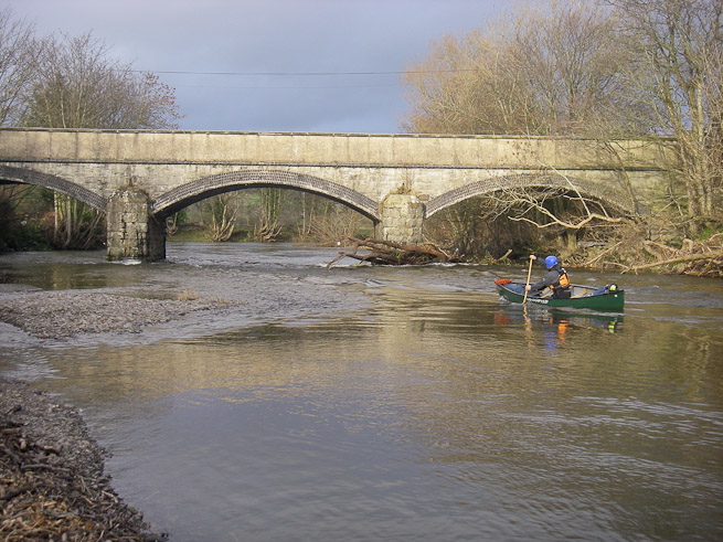 Canoeist avoiding tree caught in bridge.