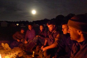 Frontier people illuminated by firelight with the moon rising.