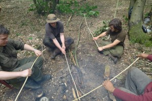 Students of bushcraft sitting around fire straightening hand drills