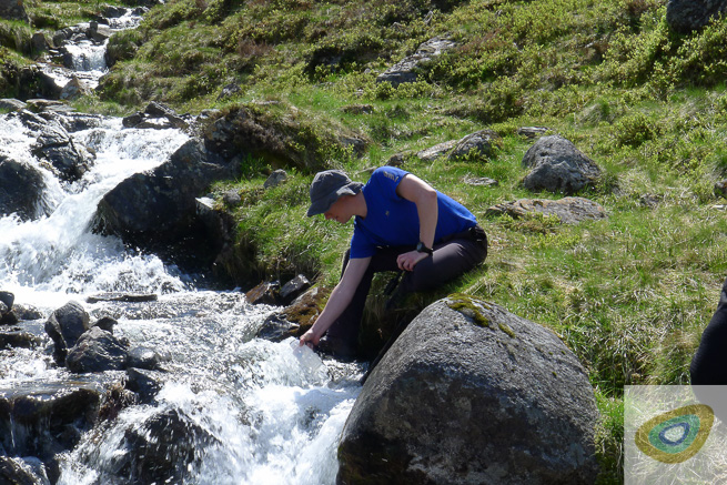 Man filling water bottle from fast flowing mountain stream