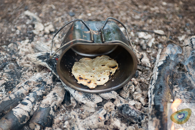 metal mug laid on campfire embers with bread cooking inside