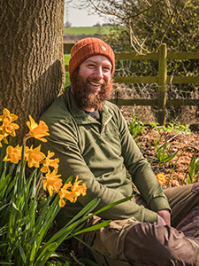 Man with good beard sitting near daffodils