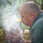 Man blowing tinder bundle with lots of smoke