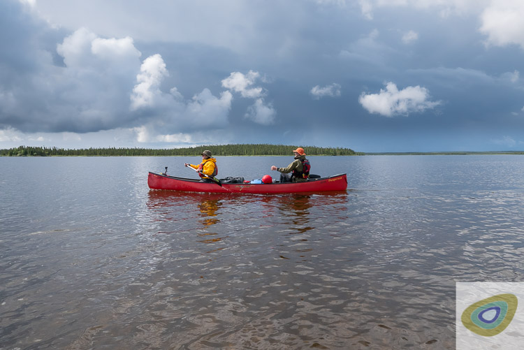 two people in canoe crossing very remote lake with ominous clouds in background