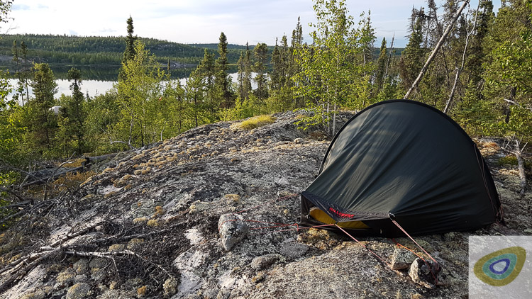 A small green tent in a vast boreal wilderness, with granite, lichens, spruces, pines