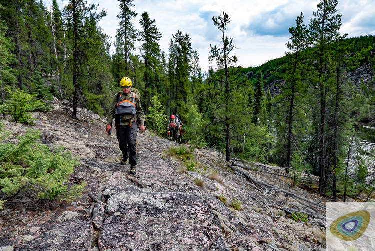 People walking up exposed bed rock slabs on a steep-sided river canyon valley, with spruces, pines and lichens